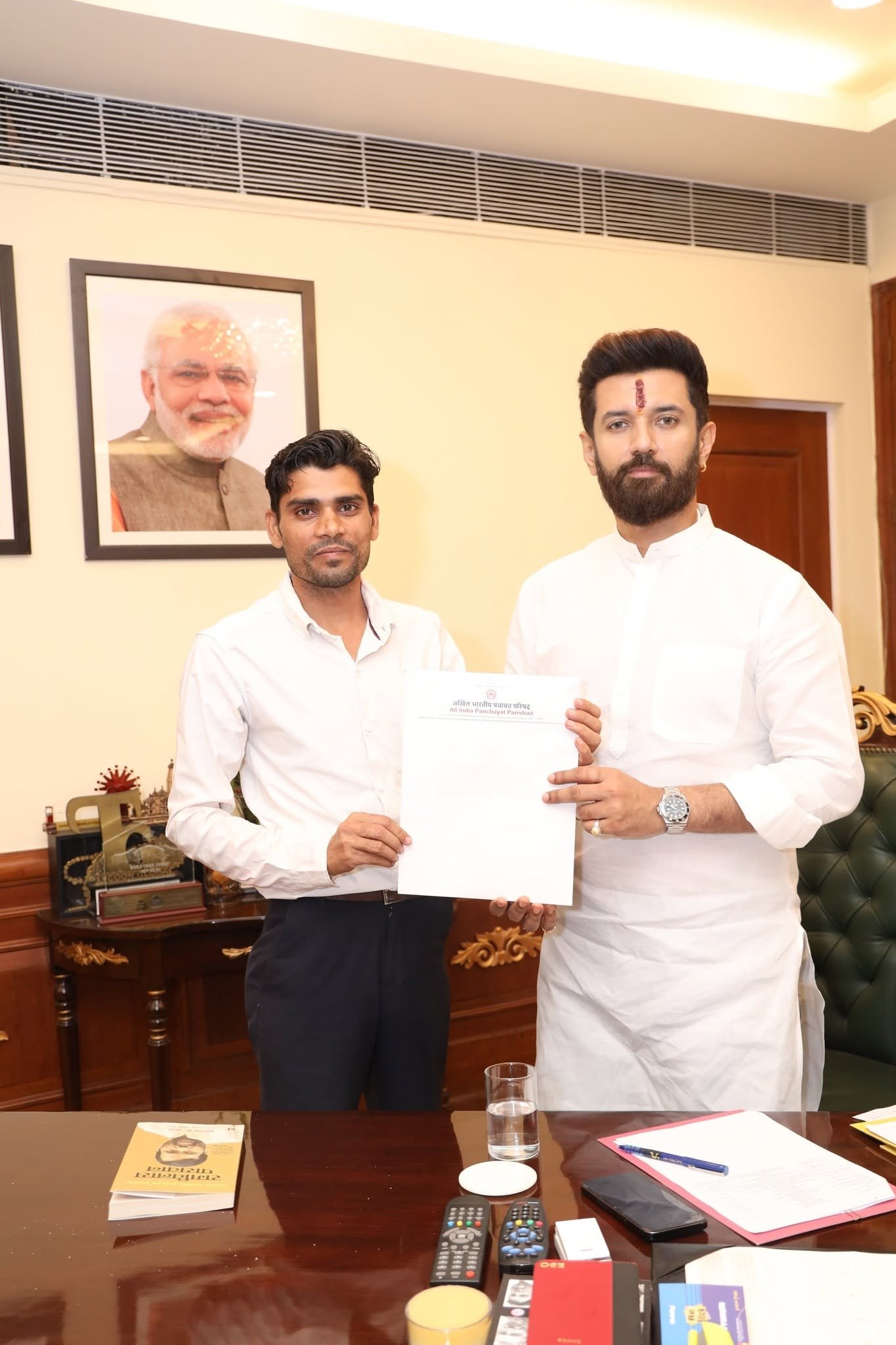Two men jointly holding an All India Panchayat Parishad letterhead document in an office
