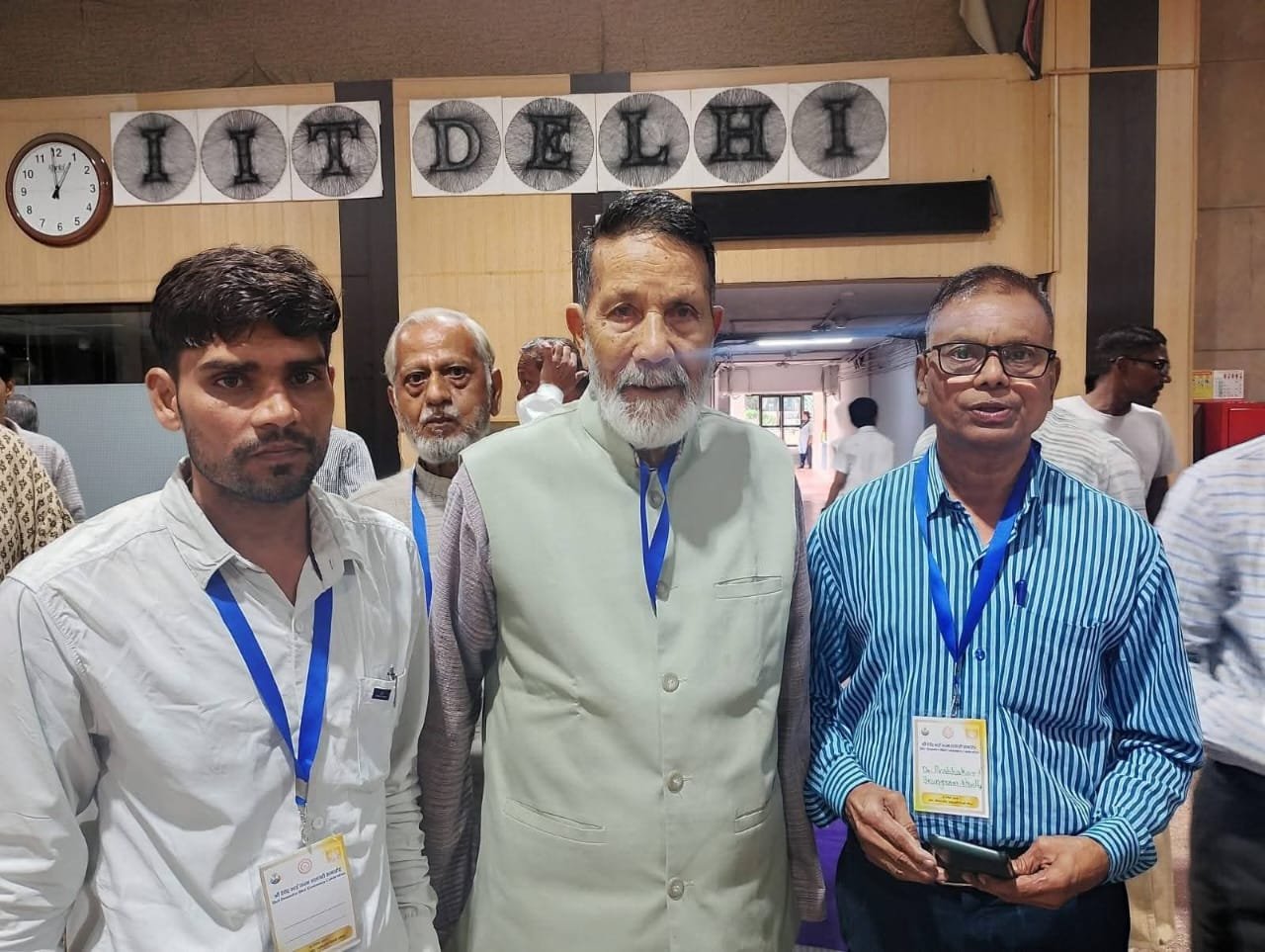 Four men wearing conference lanyards standing together in a hall